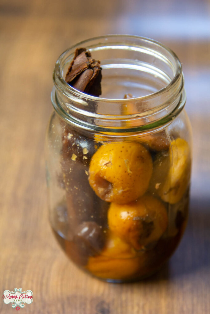 Tejocotes, guavas and a cinnamon stick inside a mason jar on top of a wooden table.