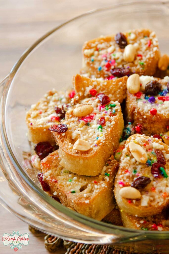 Rebanadas de pan de capirotada con chochitos, nueces y frutas secas en un tazón de cristal. 