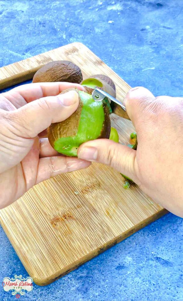 Two hands peeling a kiwi with a potato peeler. 