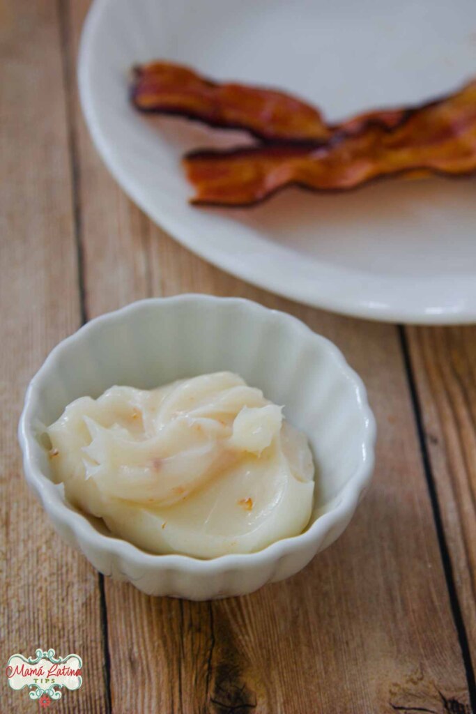 A bowl of bacon fat and a plate of bacon strips on a table.