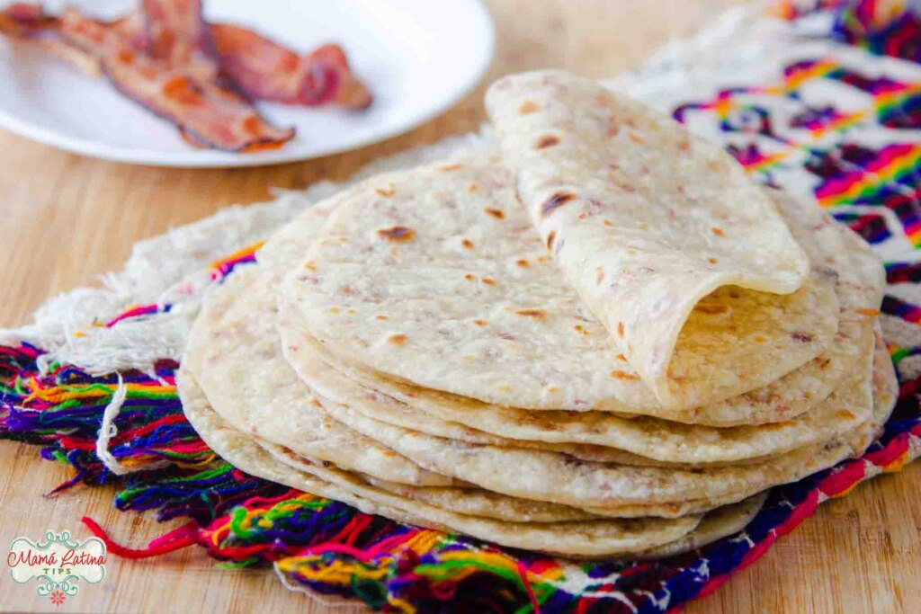 A stack of bacon fat Mexican flour tortillas on a cloth.