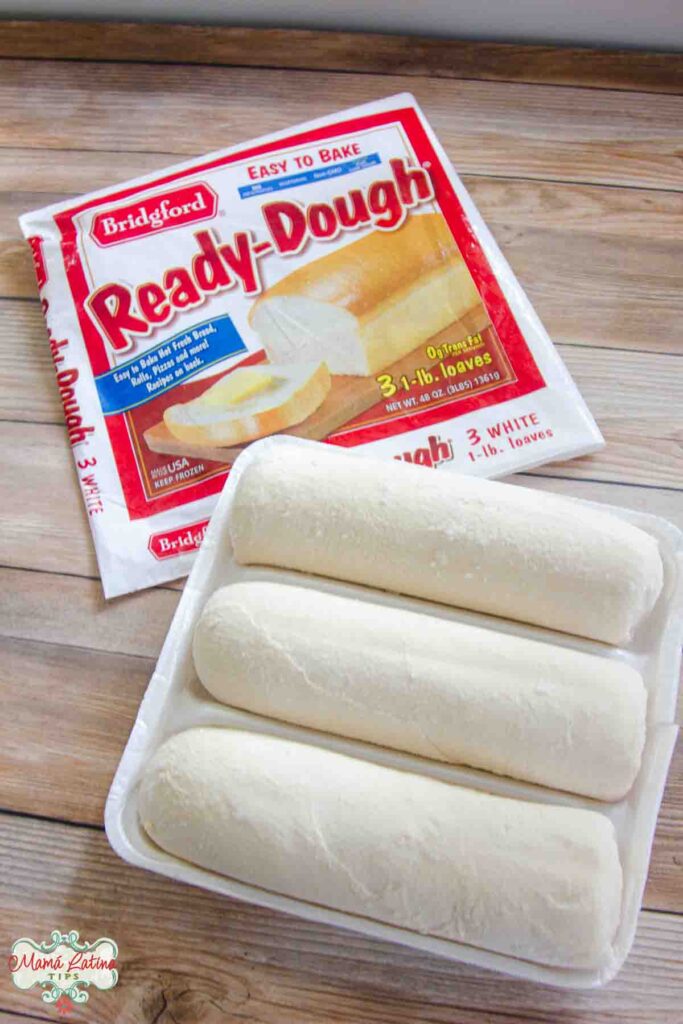 A package of Bridgford ready dough is sitting on top of a wooden table. Next to it are three frozen dough logs. 