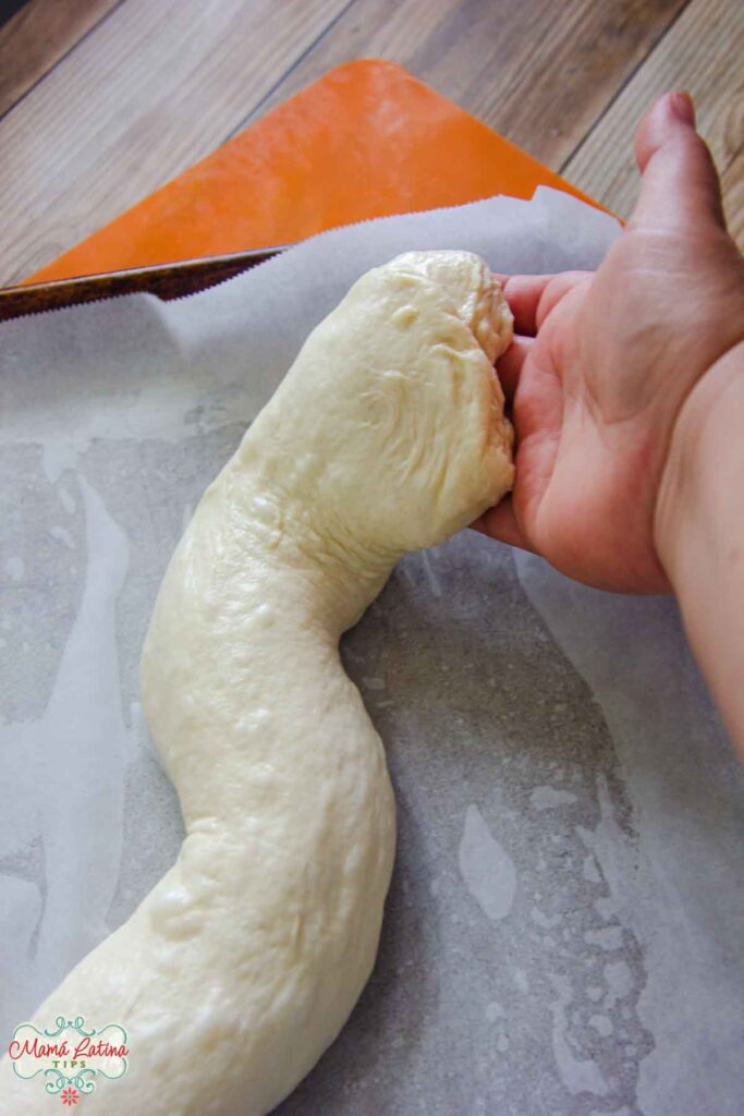 A person's hand is holding a piece of dough on a baking sheet, creating a slithery shape bread.