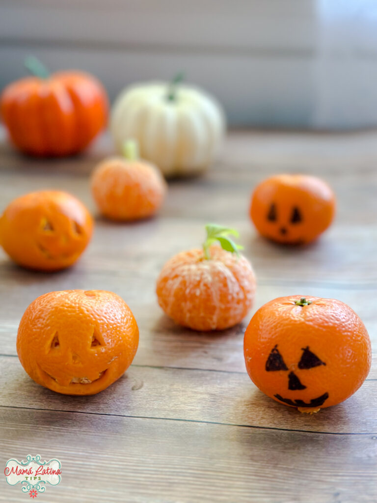 Varias mandarinas en forma de calabaza sobre una mesa de madera. Una tienen carita de Jack O'Lantern y otras tallos de apio.