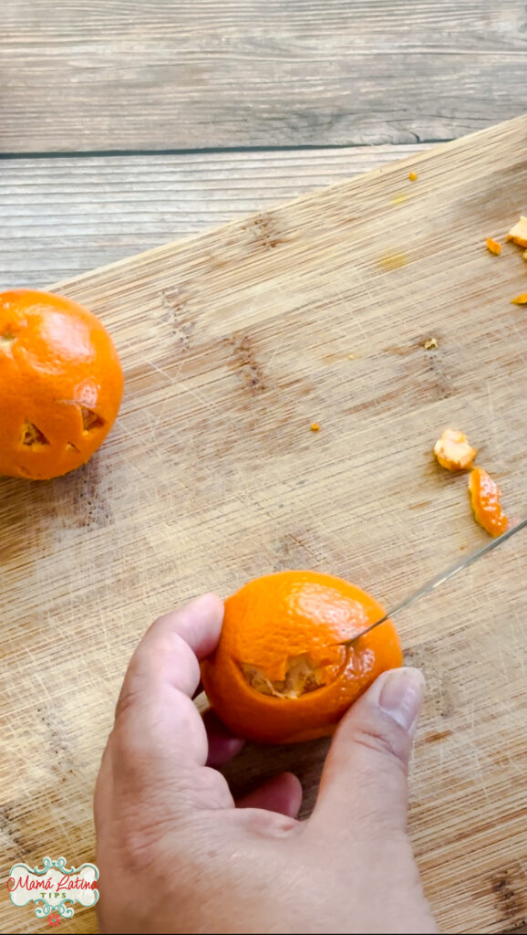 A person cutting a Jack O'Lantern face on tangerine on a cutting board.