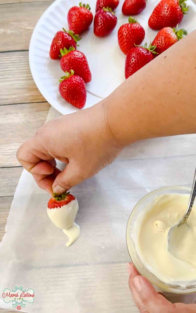 A person dipping strawberries in white chocolate and creating strawberry ghosts.