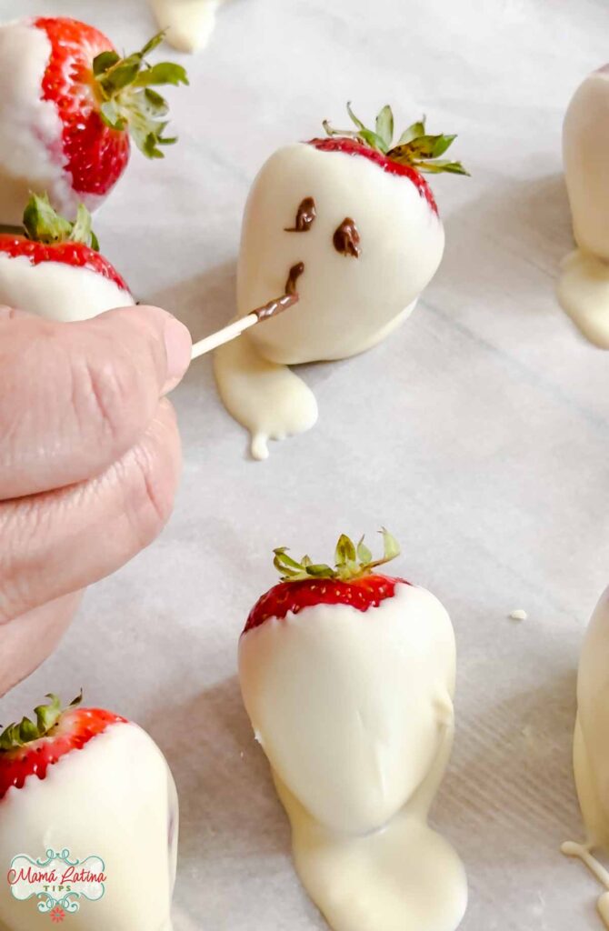 A person is decorating strawberries with white chocolate and milk chocolate.