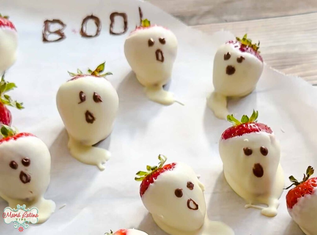 A group of ghost shaped strawberries on a baking sheet.