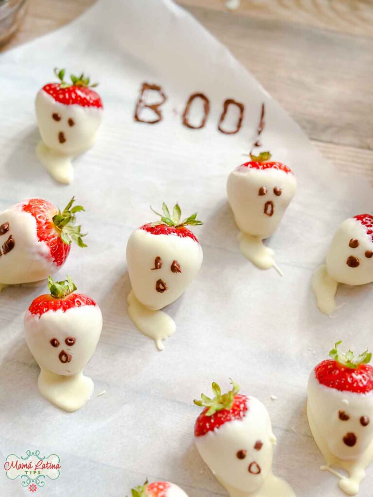 Chocolate covered strawberry ghosts on parchment paper with the word Boo! written in chocolate. 