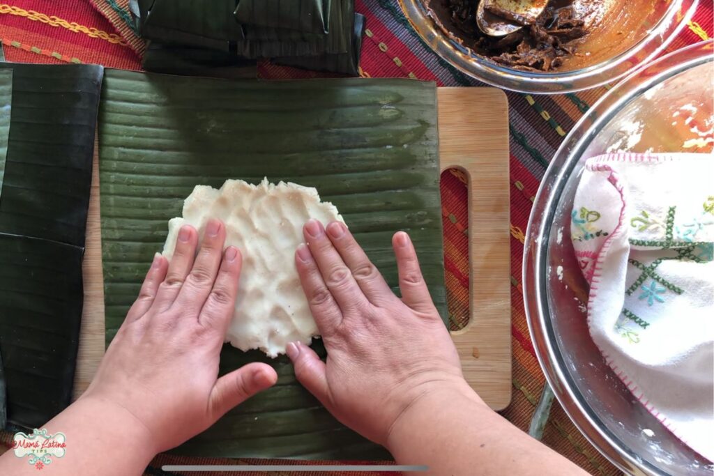 Hands placing homemade masa dough for tamales on a banana leaf.  .