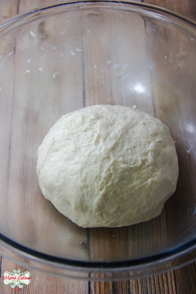 An easy homemade dough ball in a glass bowl on top of a wooden table.