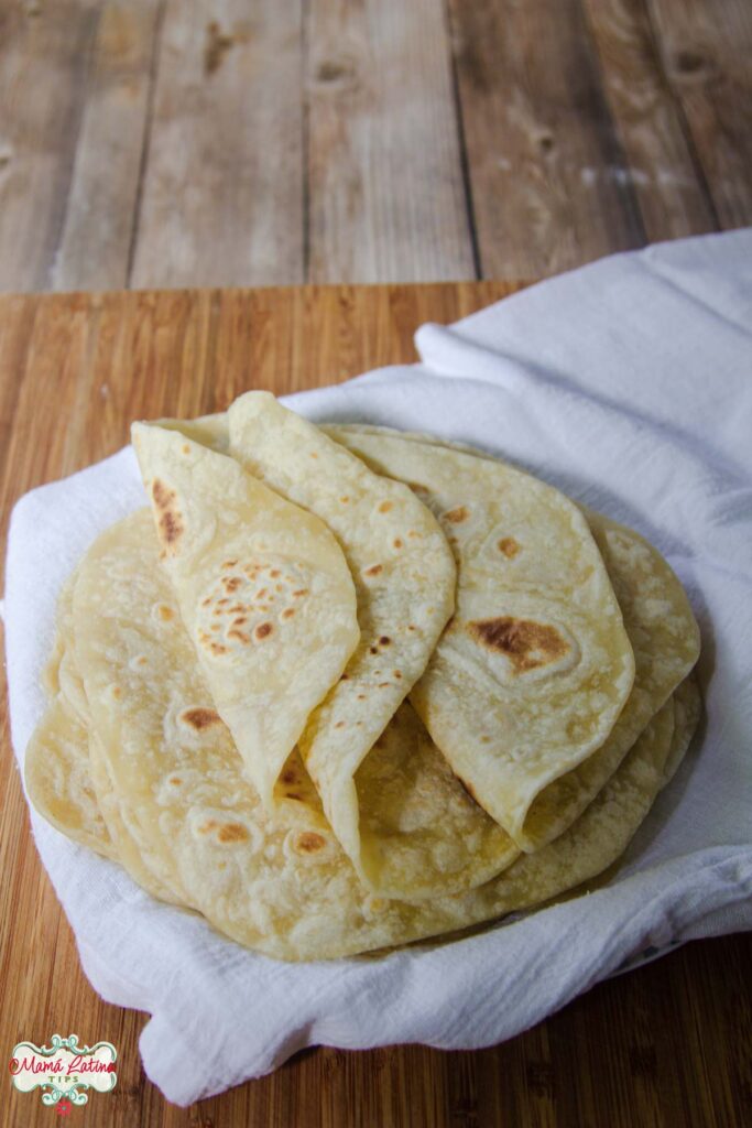 A homemade stack of flour tortillas on a wooden cutting board.