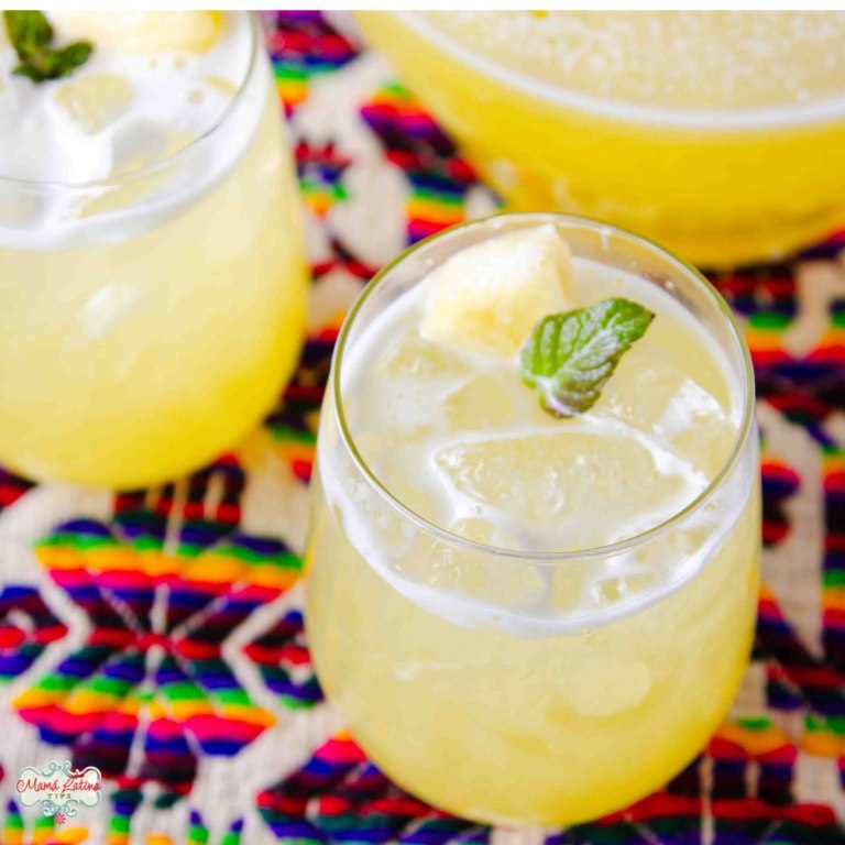 Two glasses of freshly made Pineapple Agua Fresca garnished with mint on a colorful woven cloth.