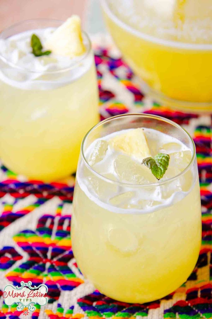 Two glasses pineapple agua fresca with ice and mint garnish on a colorful woven cloth.