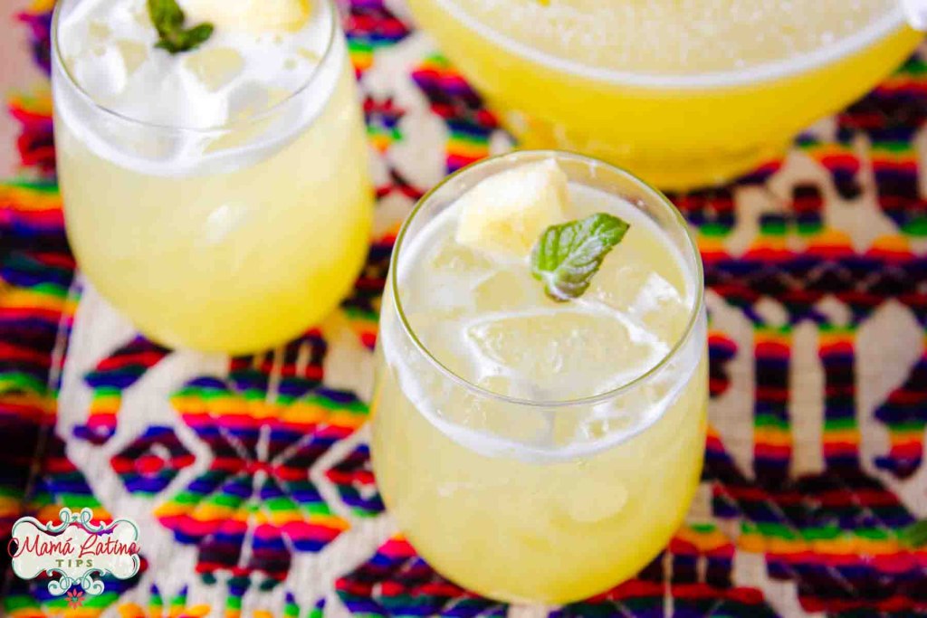 Refreshing pineapple beverages with ice and mint garnish on a colorful tablecloth.