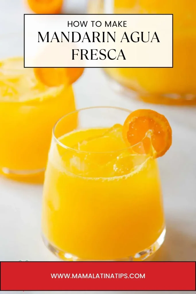 A refreshing glass of Mandarin Agua Fresca, garnished with a mandarin slice, sits in front of a pitcher and another festive glass in the background.