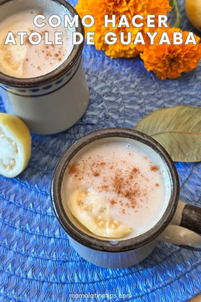 Dos tazas de atole de guayaba, una bebida tradicional mexicana, están cubiertas de canela sobre un tapete azul, rodeadas de rodajas de guayaba, flores de caléndula y una hoja de laurel. El texto dice "Como hacer atole de guayaba.
