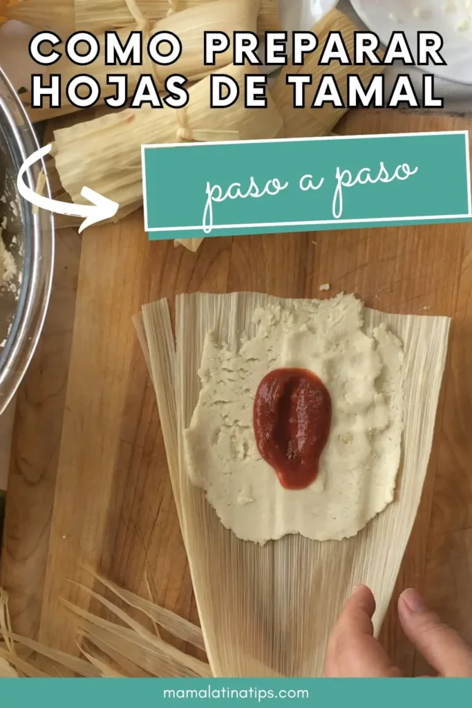 Preparación de tamales: masa untada en Hojas de Tamal con una cucharada de salsa roja, mostrada sobre una superficie de madera con más hojas y un cuenco.