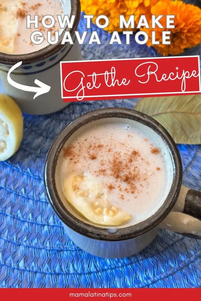Two mugs of Guava Atole, a classic Mexican drink, sit on a blue mat topped with cinnamon, with a slice of guava and marigold flowers in the background. Text reads "How to Make Guava Atole" and "Get the Recipe.