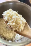 Una cuchara de madera sostiene el arroz blanco tostado sobre una olla que contiene más arroz.